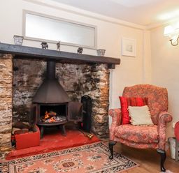 A living room with a fireplace and armchair at Yew Tree Cottage in Stoke Fleming