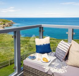 A balcony with cushions a tray with a cup an open book and a pastry overlooking the sea at Breakers in Newquay