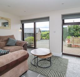 A living room with a corner sofa two nesting coffee tables and large windows overlooking an outdoor area at Cwmfadog in Llanafan-fawr near Beulah