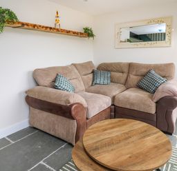 A corner sofa with cushions a round wooden coffee table and a wall shelf with plants in a living room at Cwmfadog in Llanafan-fawr near Beulah