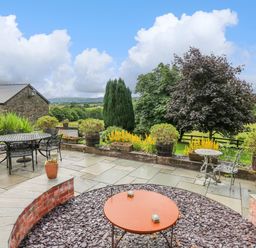 A garden patio with tables and chairs surrounded by plants and trees at Cwmfadog in Llanafan-fawr near Beulah