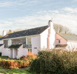 A cottage with a slate roof and pink walls surrounded by shrubs at 2 Rose Cottages Lansallos near Polperro