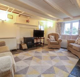 A living room with beige sofas patterned cushions a rug a TV on a stand and windows with curtains at 2 Rose Cottages Lansallos near Polperro
