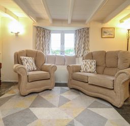 A living room with beige sofas a patterned rug and a television at 2 Rose Cottages Lansallos near Polperro