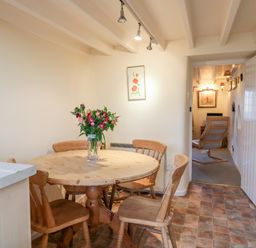 A dining area with a round wooden table and four chairs with flowers on the table at 3 Rose Cottages Lansallos near Polperro