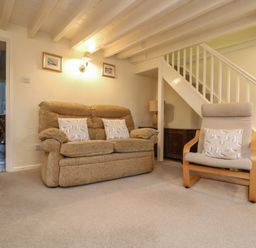 A living room with a beige sofa and armchair near a staircase at 3 Rose Cottages in Lansallos near Polperro