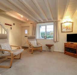 A living room with two armchairs a TV on a wooden stand and a window at 3 Rose Cottages Lansallos near Polperro