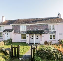A pink stone cottage with two white doors and a small garden behind a black gate at 4 Rose Cottages in Lansallos near Polperro