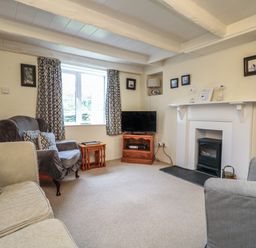 A living room with sofas a television on a wooden stand and a fireplace at 4 Rose Cottages in Lansallos near Polperro