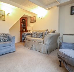 A living room with armchairs sofa cushions a corner cabinet and framed pictures on walls at 4 Rose Cottages Lansallos near Polperro
