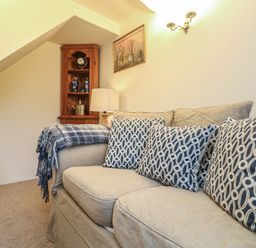 A living room with a couch patterned cushions a wooden corner shelf and a wall lamp at 4 Rose Cottages in Lansallos near Polperro