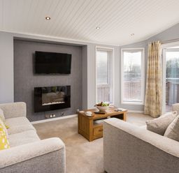 A living room with two sofas a coffee table a wall-mounted tv and a fireplace at Waternook Lodge South Lakeland Leisure Village