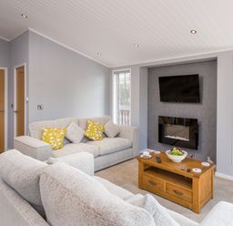 A living room with two sofas a wooden coffee table a wall mounted tv and a fireplace at Waternook Lodge South Lakeland Leisure Village