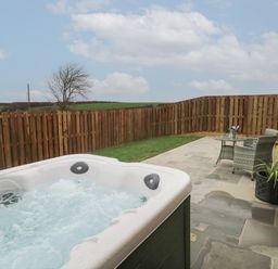 An outdoor patio with a hot tub table and two chairs next to a wooden fence and stone wall at The Cwtch in St Brides Major