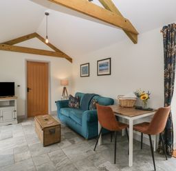 A living room with a teal sofa a wooden chest used as a coffee table a small dining table with two chairs and a TV on a cabinet at The Cwtch in St Brides Major