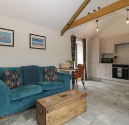 A living room with a blue sofa wooden chest coffee table kitchen in the background and a dining table with chairs at The Cwtch in St Brides Major