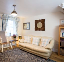 A living room with a cream sofa and rocking chair near a window with curtains at Old Post Office in Bull Bay