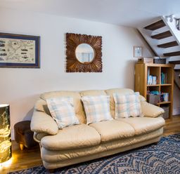 A living room with a beige sofa and three checkered pillows a wooden bookshelf under stairs a standing lamp and wall decorations at Old Post Office in Bull Bay