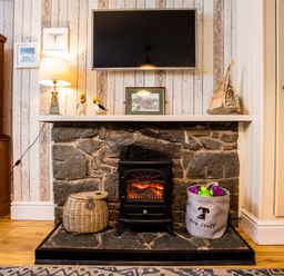 A stone fireplace with a small stove and baskets on each side below a mounted television and lamp in a sitting room at Old Post Office Bull Bay