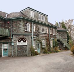 A stone building with teal doors and stairs surrounded by bushes and trees at Sethera in Ambleside