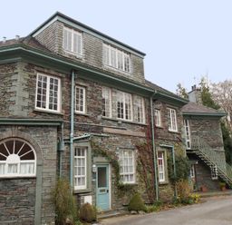 A stone building with multiple windows green doors and an external metal staircase surrounded by plants and trees at Sethera in Ambleside