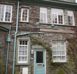 The stone exterior of a building with multiple white-framed windows and a blue door with climbing plants at Sethera in Ambleside
