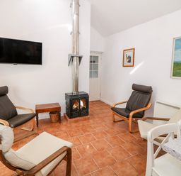 A sitting room with four armchairs a small wooden table a wood burning stove and a wall mounted television at Y Buarth in Waunfawr