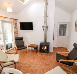 A sitting room with armchairs a wood burning stove a wall mounted tv and sliding glass doors at Y Buarth in Waunfawr