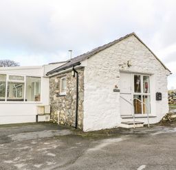 A stone and white painted cottage with a small porch and a mailbox outside at Y Buarth in Waunfawr