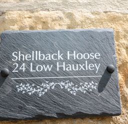 A black rectangular plaque with white text mounted on a textured stone wall reading Shellback Hoose 24 Low Hauxley at 24 Hauxley Links in Low Hauxley near Amble