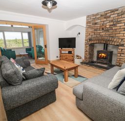 A living room with two grey sofas a wooden coffee table a wood burning stove set in a brick fireplace and a television at 24 Hauxley Links Low Hauxley near Amble