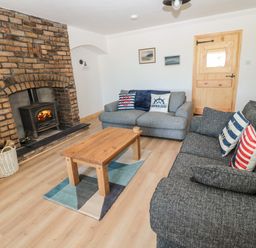 A living room with two sofas a wooden coffee table a brick fireplace and a wooden door at 24 Hauxley Links in Low Hauxley near Amble