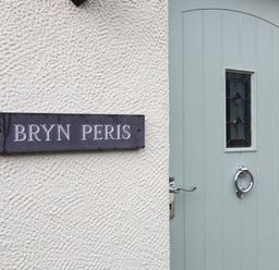 A wall with a sign reading Bryn Peris next to a light blue door with a small window at Bryn Peris in Moelfre