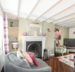 A living room with a fireplace a grey chair with cushions a green armchair and a television at Bryn Peris in Moelfre
