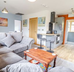 A living room with grey sofas a wooden coffee table and an open kitchen with bar stools at Bryn Hyfryd in Harlech