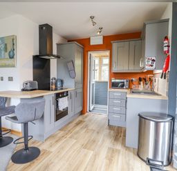 A kitchen with grey cabinets a breakfast bar with two stools and an orange wall at Bryn Hyfryd in Harlech