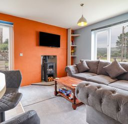 A living room with a grey sofa a wooden coffee table a wall-mounted TV and a stove at Bryn Hyfryd in Harlech