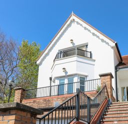 A white house with a red roof and black railings next to a staircase and trees at Cambrie in Tenby