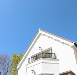 Exterior view of a white house with a small balcony and a sloped roof under a clear blue sky at Cambrie in Tenby