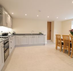 A kitchen with gray cabinets and a dining table with wooden chairs and flowers at Hen Dy Bryn Mawndy Melin y Wig near Corwen