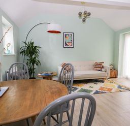 A living room with a wooden table and chairs a beige sofa colorful rug and a tall plant at Robins Nest Cottage in Brandesburton