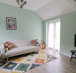 A living room with a beige sofa with patterned pillows a colorful geometric rug a TV on a stand and a round wooden side table at Robins Nest Cottage in Brandesburton
