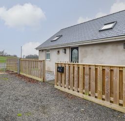 A gravel driveway with a wooden fence and gate in front of a house with a gray slate roof at 3 Mountain View in Talwrn near Llangefni