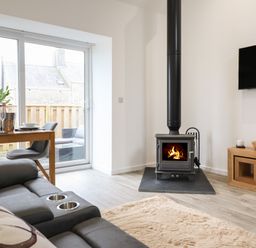 A living room with a wood stove a sofa a dining table with chairs and a wall-mounted television at 3 Mountain View in Talwrn near Llangefni