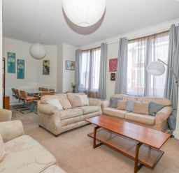 A living room with beige sofas a wooden coffee table and large windows at Victorian Town House in Weymouth