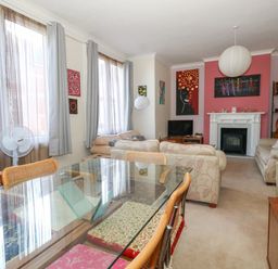 A living room with sofas dining table glass top and paintings on the wall at Victorian Town House in Weymouth