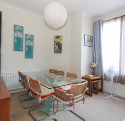 A dining room with a glass table and six chairs next to a window with curtains and a standing fan Victorian Town House Weymouth