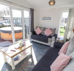 A living room with two sofas a coffee table and sliding glass doors leading to a patio with a hot tub at Duckling Lodge in South Lakeland Leisure Village