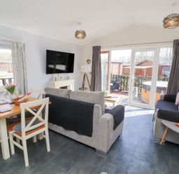 A living room with sofas a dining table a wall mounted television and glass doors leading outside at Duckling Lodge in South Lakeland Leisure Village