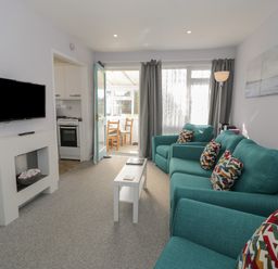 A living room with teal sofas and multicolored cushions with a white coffee table and a wall-mounted TV at Hafod-y-Gors in Fairbourne